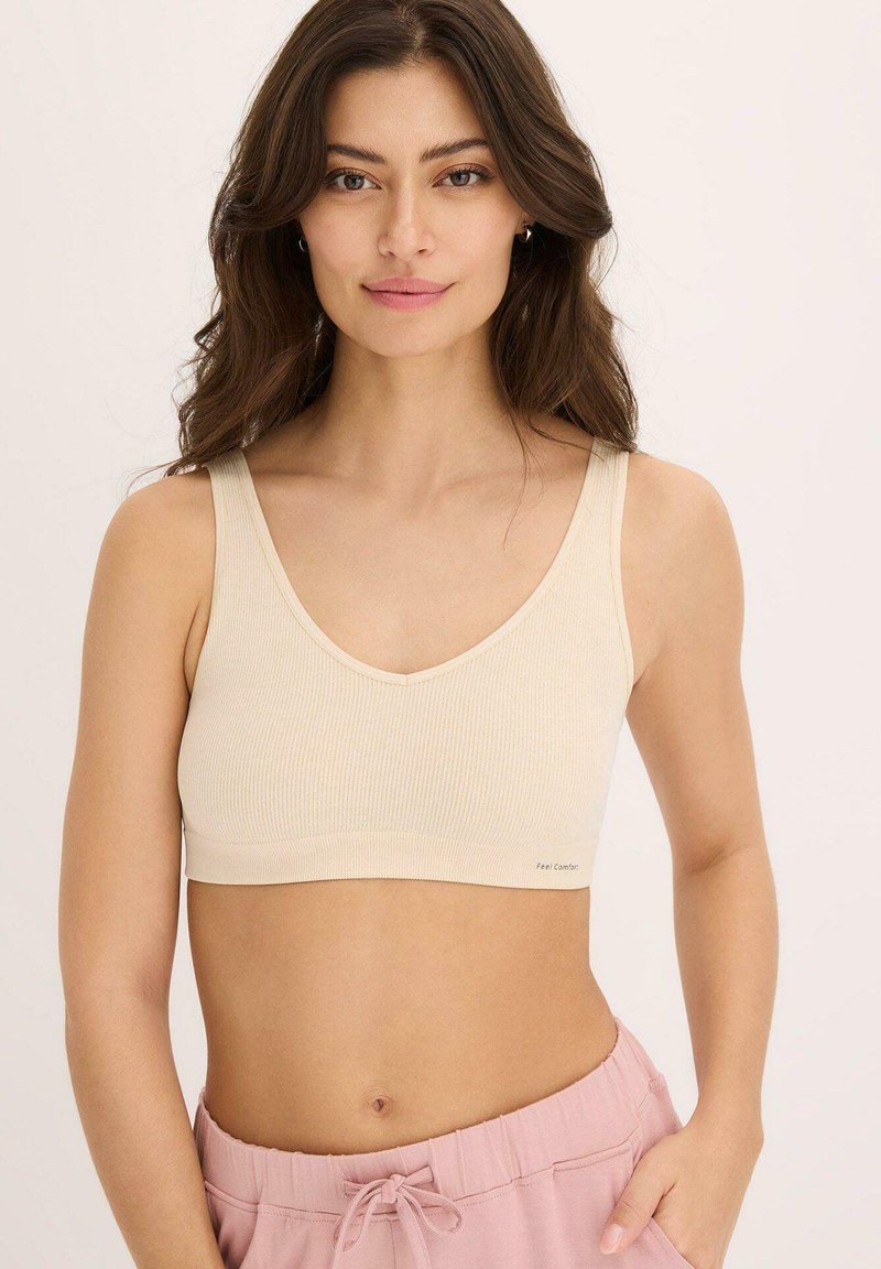 Bralette a coste di un leggero beige con spalline larghe e scollatura a V, caratterizzato da una texture liscia e branding minimale vicino all'orlo.