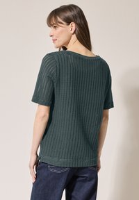 Top verde lavorato a maglia con maniche corte, caratterizzato da una trama a maglia larga e un ampio scollo. Ha una vestibilità comoda e spacchi laterali all'orlo.