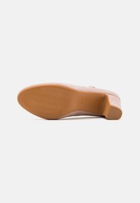 Scarpa con tacco alto in suede beige, punta rotonda e suola in gomma con un motivo testurizzato. Il tacco visibile offre un'altezza aggiuntiva.