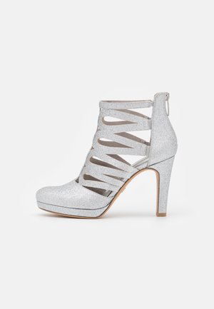 Silver glitter high-heeled ankle boot with cut-out design, pointed toe, and a back zipper. Features a platform sole and textured surface.