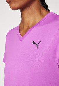 Lühikeste varrukatega lilac värvi V-kaelusega T-särk, mille vasakul rinnal on must Puma logo. Sile tekstuur, lõdvestunud disain.