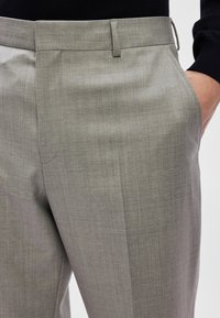 Calças cinza claro feitas de um tecido texturizado. Apresentam um acabamento liso, corte ajustado, bolsos laterais e design de frente lisa.