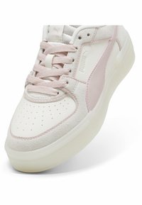 Vit sneaker med ljusrosa accenter, detaljer av mocka och läder, perforerad tå, rosa snörning och tjock transparent sula.
