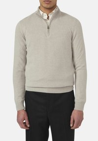 Lichtbeige gebreide pullover met een kwart-rits kraag, ribgebreide manchetten en zoom, lange mouwen en een gladde textuur. Gecombineerd met zwarte broeken.