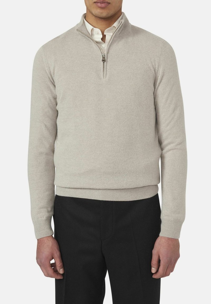 Lichtbeige gebreide pullover met een kwart-rits kraag, ribgebreide manchetten en zoom, lange mouwen en een gladde textuur. Gecombineerd met zwarte broeken.