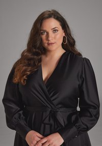 Vestido envolvente de satén negro con escote en V profundo y mangas abullonadas. Presenta una cintura atada y detalles de botones en los puños. Textura suave.