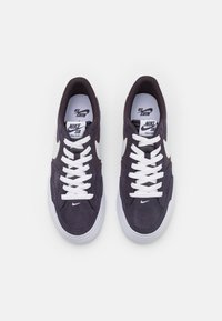 Nike SB sneakers feature a navy suede upper, white laces, and a white swoosh logo. The sole is white with a rounded shape.