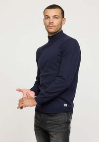 Pull à col roulé bleu marine en tricot doux, au design ajusté avec des manches longues et une petite étiquette logo près de l'ourlet.