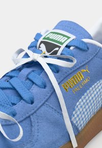 Plave zakupne tenisice s bijelim vezicama, zlatnim "PUMA" logom i detaljem od kariranog platna. Ravni potplat s teksturiranom površinom za bolje prianjanje.