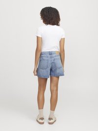 Shorts en denim bleu clair, avec une taille haute, un ourlet effiloché et des poches arrière. Associés à un t-shirt blanc ajusté et des baskets beiges.