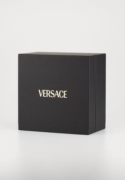 Melns kartona kastīte ar teksturētu apdari, kuras priekšpusē ir zelta iegriezts "VERSACE" logo. Vienkāršs taisnstūra dizains.