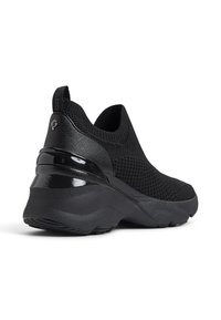 Black slip-on sneakers featuring a mesh upper, a textured heel with a shiny accent, and a thick, contoured rubber sole.