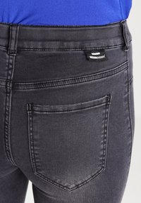 Dark gray denim jeans with a back pocket and a brand label near the waistband. The fabric appears smooth with subtle texture.