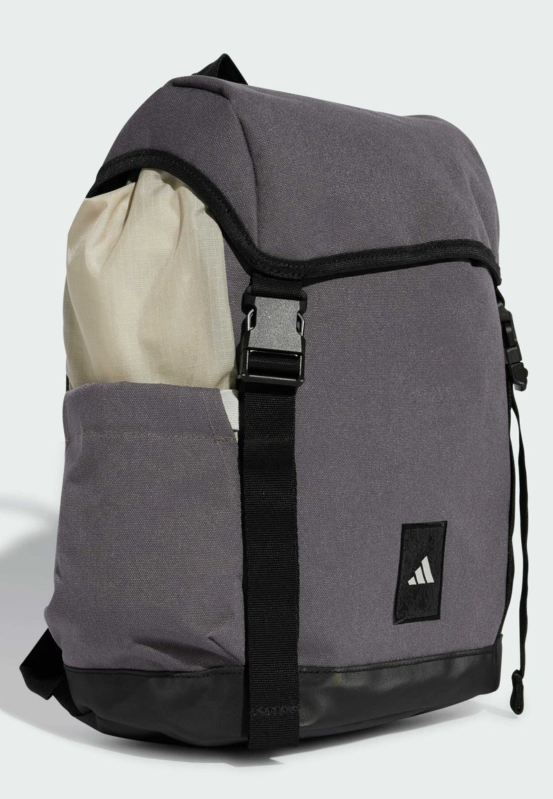 Grauer Stoff-Rucksack mit strukturierter Oberfläche, schwarzen Akzenten, verstellbaren Trägern und einer Außentasche für zusätzlichen Stauraum.