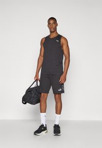 Zwarte mouwloze tanktop en shorts, beide met een Puma-logo, gecombineerd met zwart-witte sneakers en een zwarte sporttas.