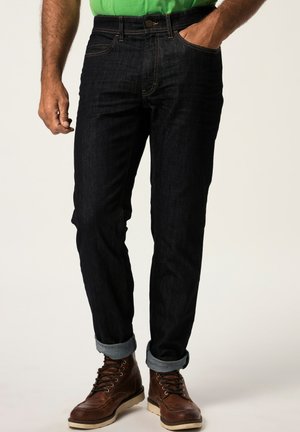 Dark blue denim jeans with a slim fit, featuring light stitching, five pockets, and rolled cuffs. Paired with brown boots.