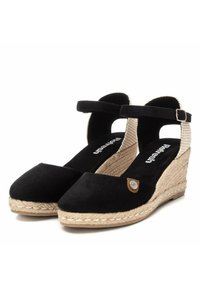 Espadrilles de charol negro con cuña trenzada, tira de tobillo de tejido, tacón de yute envuelto y un pequeño acento metálico en el lado.