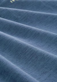 Niebieski materiał tekstylny o miękkiej, teksturowanej powierzchni, z subtelnym wzorem melanżu i delikatnymi fałdami, co wskazuje na lekki i elastyczny materiał.