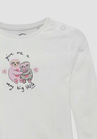 Twee glimlachende luiaards die elkaar omarmen met roze harten, omringd door bloemen, en de tekst "geef me een heel grote KNUFFEL" op een witte lange mouw shirt.