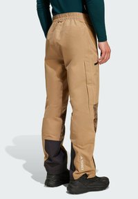 Bež hlače otporné na vodu s opuštenim krojem, s bočnim džepovima, crnim akcentima na rubovima i uzorkovanim panelima sa strane.