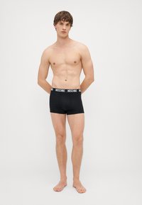 Mustad mustad pokud, millel on pehme vöökoht, millel on Moschino logo. Kangas näeb välja veniv ja sile, loodud mugavuseks.