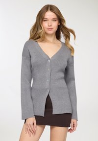 Cardigan grigio in maglia con scollo a V, chiusura con cinque bottoni, maniche lunghe, texture a coste e orlo dritto con spacchi laterali.