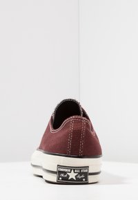 Zapatilla de lona burdeos con suela de goma blanca, costuras en blanco en contraste y detalles negros en el talón con la inscripción "Converse All Star."