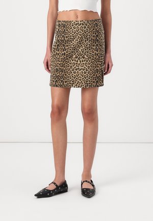 Mini gonna in tessuto leopardato nei toni del marrone e del nero. Presenta un design aderente, una texture liscia e un orlo dritto. Indossata con scarpe nere basse.
