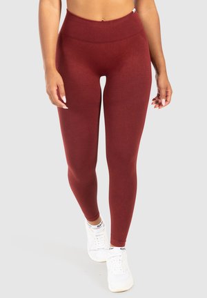 Leggings taille haute rouges avec une finition texturée et un design sans couture, associés à des baskets blanches. Les jambes sont ajustées et lisses.