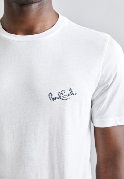 Valge lühikeste varrukatega T-särk, mis on valmistatud pehmest kangast, sinise tikandiga "Paul Smith" logoga vasakus rinnaosas.