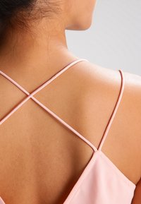 Rosa ärmlös topp med tunna korsryggsremmar, som visar en slät tygtextur och en närbild av nacköppningen och axelområdet bak.