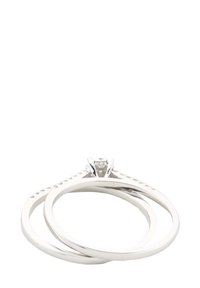 Tres anillos de plata entrelazados con superficies pulidas. Uno presenta una gema central con un engaste de garras y acentos texturizados a lo largo de la banda.