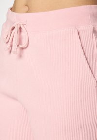 Pantalons côtelés rose clair avec un tissu texturé, une taille élastique et un cordon de serrage, dotés de deux poches latérales.
