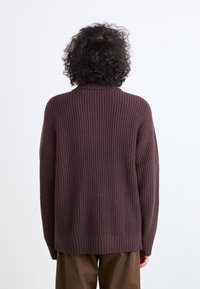 Brauner gerippter Strickpullover mit hohem Kragen und langen Ärmeln. Verfügt über eine lockere Passform und eine einheitliche Farbe.