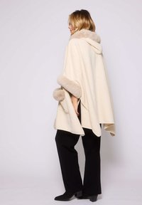 Capa color crema con capucha, con un suave borde de piel de color beige en los bordes y las mangas; combinada con pantalones negros y botas.