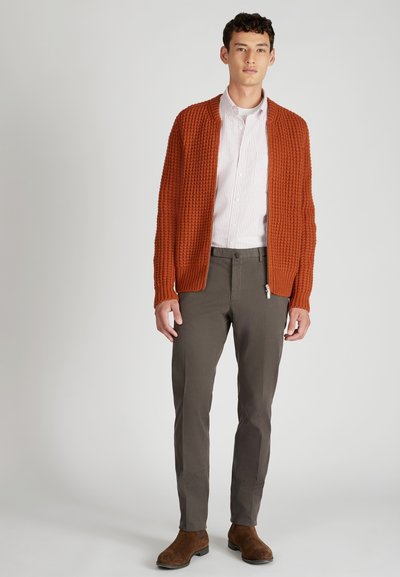 Rdzawo-pomarańczowy sweter dziany na białej i różowej koszulce w paski, w zestawieniu z dopasowanymi szarymi spodniami i brązowymi zamszowymi botkami za kostkę.