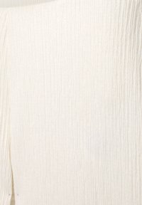 Tissu blanc à côtes avec une texture verticale visible et un motif de tissage subtil, montrant un gros plan de la surface du matériau.