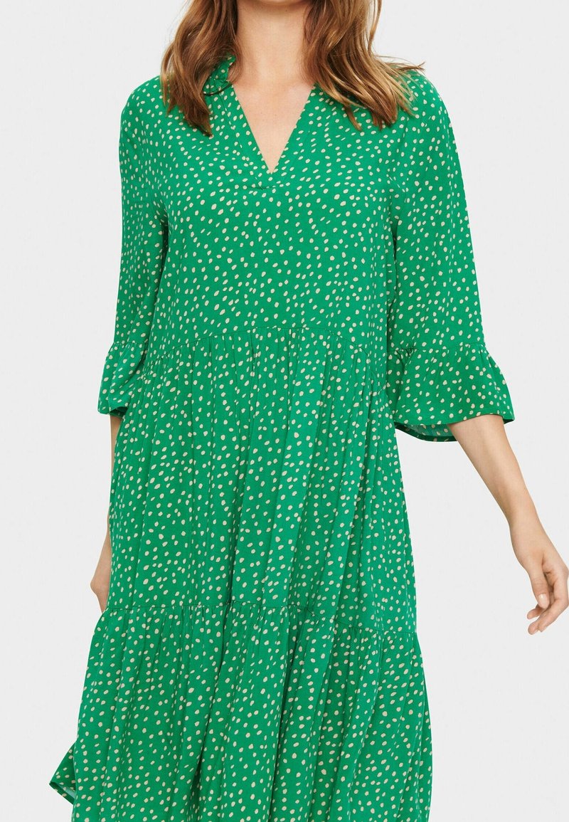 Zelené šaty s výstřihem do V, tříčtvrtečními rukávy, vrstveným designem a bílými puntíky. Vyrobené z lehkého materiálu s vláčnou texturou.