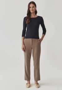 Granatowy sweter z dzianiny z rękawami o długości trzech kwart, w połączeniu z beżowymi spodniami w kant z bocznymi kieszeniami. Beżowe płaskie buty.