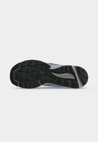 Σόλα μπλε και γκρι παπουτσιού για τρέξιμο New Balance με μαύρο ανάγλυφο σχέδιο και το όνομα της μάρκας στη μεσαία σόλα.