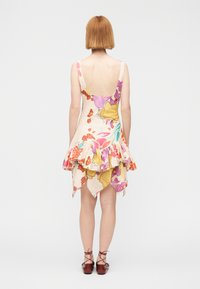 Φόρεμα με λουλουδάτο σχέδιο, ανοιχτή πλάτη, βολάν στο στρίφωμα και ασύμμετρο σχήμα. Κατασκευασμένο από ελαφρύ ύφασμα σε παστέλ αποχρώσεις. Φορεμένο με καφέ παπούτσια.