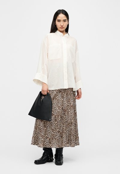 Διάφανη λευκή πουκαμίσα με κουμπιά και δύο τσέπες, συνδυασμένη με φούστα μεγάλου μήκους καφέ με λεοπάρ σχέδιο και υφασμάτινη μαύρη τσάντα. Μαύρα μποτάκια αστραγάλου.