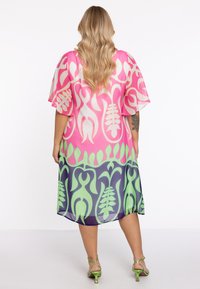 Kaftan multicolore avec un motif floral ; présente des couleurs rose, verte et marine ; tissu léger et fluide ; manches larges.