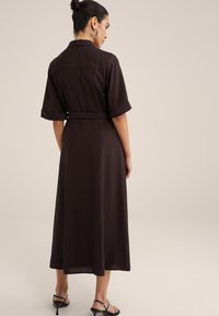 Rochie brună, de lungime medie, cu guler, mâneci scurte rulate, talie cu brâu și un design fluid, realizată dintr-un material ușor.