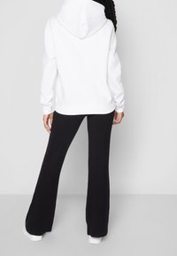 Felpa bianca con cappuccio, dal fit rilassato, abbinata a pantaloni neri a campana a costine e sneakers bianche, vista da dietro.