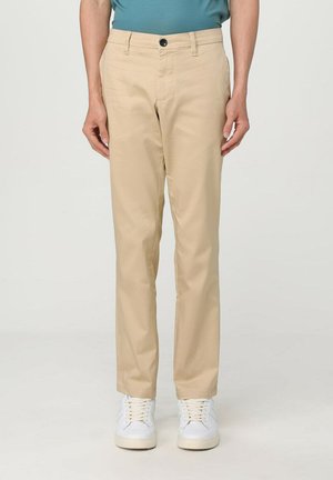 Pantaloni beige in tessuto liscio, con chiusura frontale a bottone, due tasche laterali e design slim fit. Indossati con sneaker bianche.
