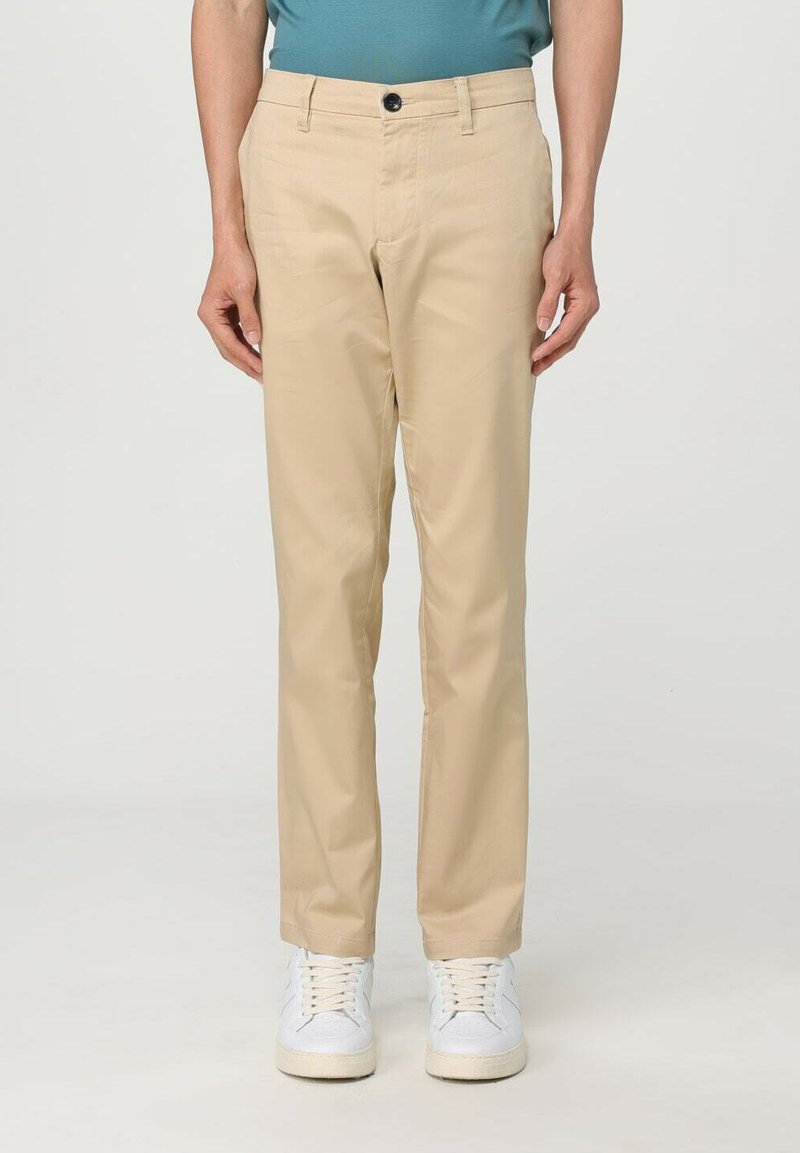 Pantaloni beige in tessuto liscio, con chiusura frontale a bottone, due tasche laterali e design slim fit. Indossati con sneaker bianche.