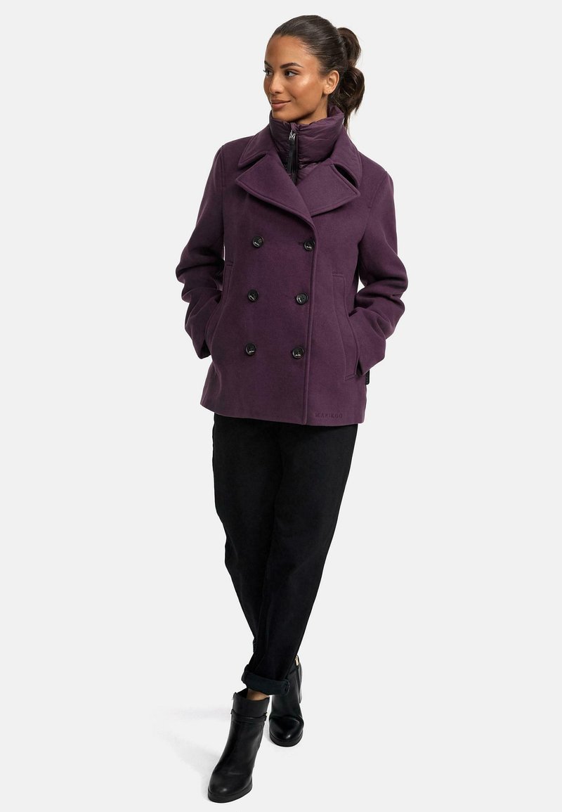 Lila dubbelknäppt kappa med svarta knappar och breda slag. Bärs med svarta byxor och ankle boots. Slät textur och strukturerad design.