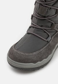 Botas grises impermeables que presentan una combinación de material sintético suave y ante suave. Tienen una suela de goma para tracción y acentos cosidos.