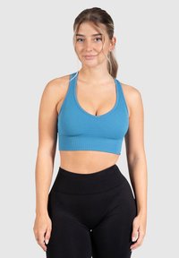 Sostenedor deportivo azul con acanaladuras, escote redondeado y tirantes anchos, combinado con leggings negros de cintura alta. Textura sin costuras y diseño ajustado.